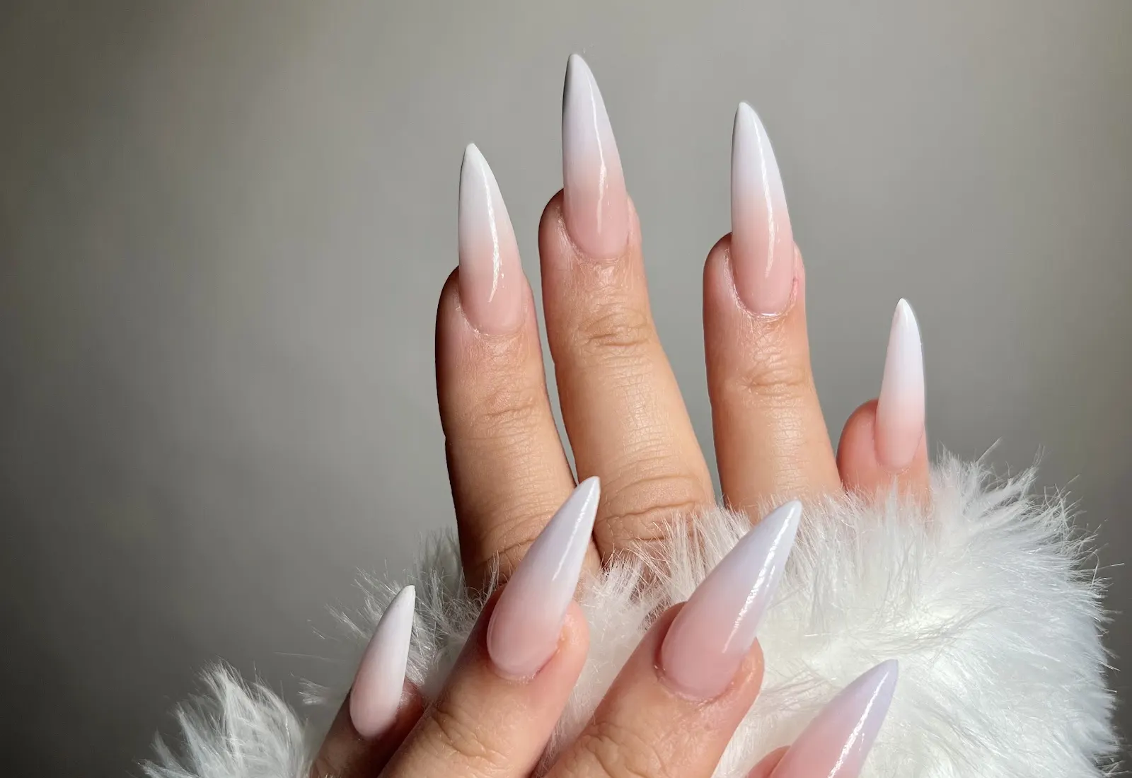 Long ombre stiletto nails resting on white fur