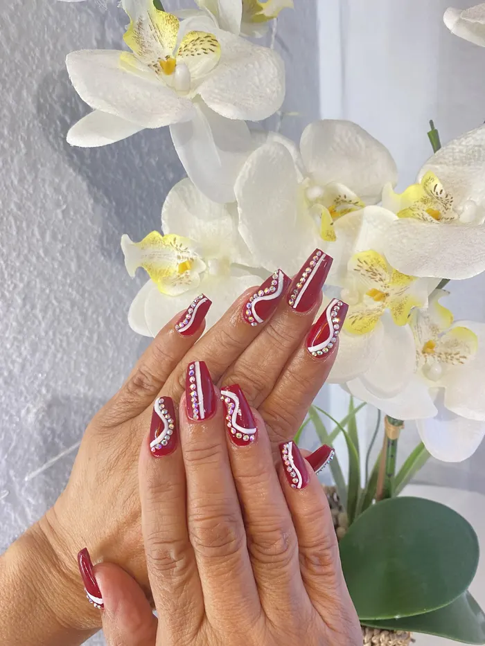 Deep red nails with rhinestones beside orchids